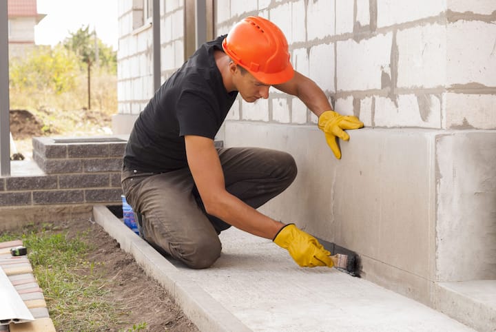 A contractor performs waterproofing on concrete.